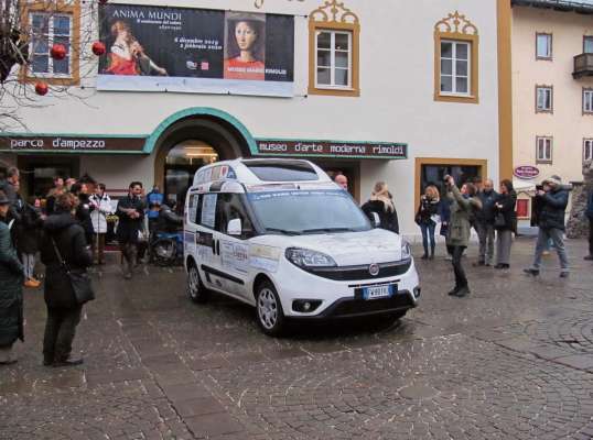 L ea un grun de śente in piaza, a vede el furgon noo da dorà par fei viaśà ra parsones che stenta a se moe. Un projeto pagà da tropa aziendes de Anpezo e de i paesc śo par pede.
