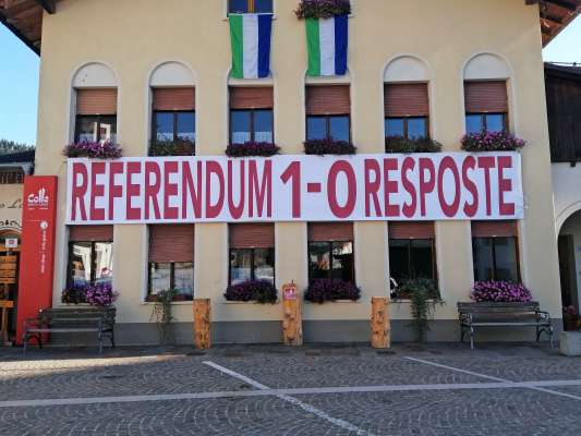 L placat tacà fora ai 29 de otobre su le vege scole da Col, per regordà che che la jent l suo la l à fat, ma la politica ncora la tas.
