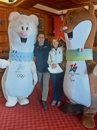 Ra doa mascotte de ra Olimpiades e de ra Paralimpiades d’inverno 2026, in Ciaśa de Comun de Anpezo, con el capocomun anpezan Gianluca Lorenzi e ra so vize Roberta Alverà.
