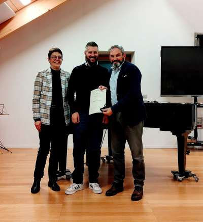 La presidenta Cristina Moser e l diretor Roberto Silvagni premia l bandist e raprejentant de la Federazion Adriano Winterle.
