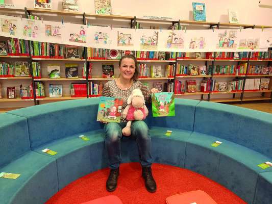 Isabella Halbeisen cun la mascotte »Wolli« tla biblioteca de Sëlva. 
