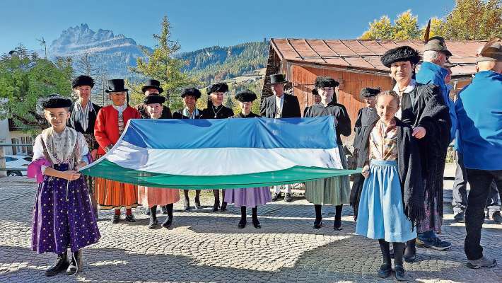 Ra bandiera ladina co i tre colore de ra Dolomites, portada da femenes e pizores co i sarvije da canpanoto.
 Ra bandiera ladina co i tre colore de ra Dolomites, portada da femenes e pizores co i sarvije da canpanoto.
