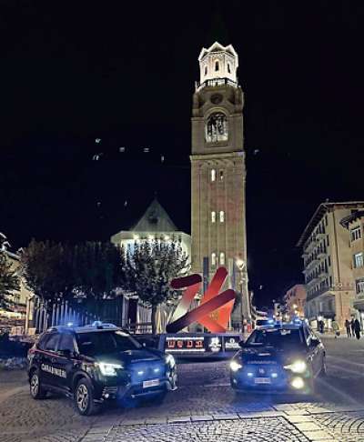 Melitare e machines de i Carabiniere in Anpezo, inze ra piaza, sote el cianpanin, daante a ‘l arloio de ra Olimpiades che ‘s é drio a ruà.
 Melitare e machines de i Carabiniere in Anpezo, inze ra piaza, sote el cianpanin, daante a ‘l arloio de ra Olimpiades che ‘s é drio a ruà.
