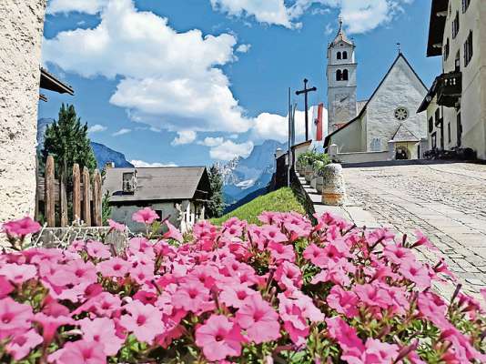 La Vila, co la bela gesia sunsom l col, d&rsquo;ist&agrave; via semper abelida con fiori de marevea. (&copy; Colle Santa Lucia-Dolomiti)
